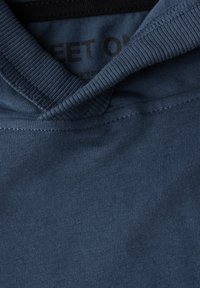 Mörkblå bomullströja med ribbad krage. Tyget visar en jämn textur, med en synlig etikett inuti som säger "SWEET ON."