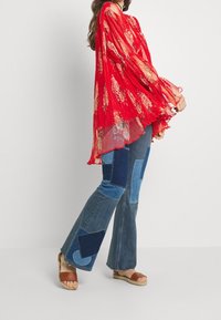 Punainen laskostettu paita, jossa on kukkakuosi; reilu malli. Yhdistetty sinisävyisiin tilkkutäkkifarkkuihin. Vaaleat espadrillot täydentävät asua.