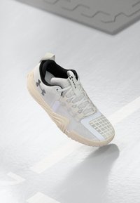 Weiße Sportschuh mit einer strukturierten Mesh-Oberfläche, einem schwarzen Innenraum und einer beigen Gummisohle mit einem gemusterten Grip. Akzentuiert durch subtile Details.