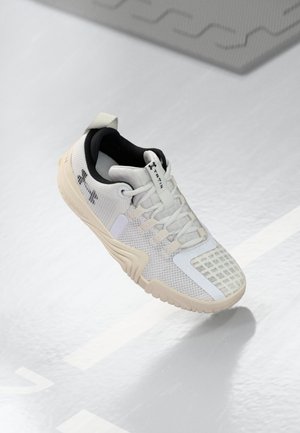 Scarpa sportiva bianca con una tomaia in mesh testurizzato, un interno nero e una suola in gomma beige con una presa a motivo. Accentuata da dettagli sottili.