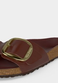 Καφέ δερμάτινο σανδάλι Birkenstock με φαρδιά λουράκι, μεγάλη χρυσή αγκράφα και φελλό πάτο.