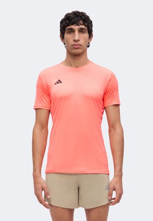 Bărbat purtând un tricou sport cu mânecă scurtă de culoare coral aprins și pantaloni scurți bej, stă în picioare cu fața înainte și cu o expresie neutră.