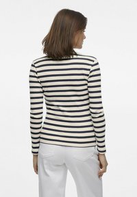 Långärmad topp i ribbat tyg med marinblåa och vita horisontella ränder. Har en rundad halsringning och en FIGURKRAMANDE SILUETT. Bärs med ljusa byxor.