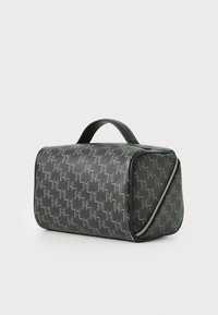 Grå mønstret sylinderformet veske med en teksturert overflate, svarte skinnakenter, et håndtak på toppen og en sidelukking med glidelås.