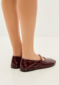Burgundylacklederschuhe mit runder Zehenform und einem kleinen verstellbaren Schnallenriemen vorne. Schmale schwarze Gummisohle.