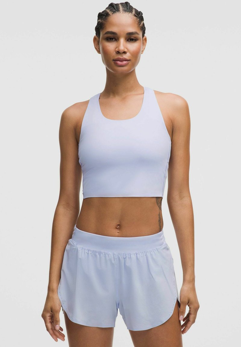 Světle fialový sportovní crop top a odpovídající šortky vyrobené z hladkého, elastického materiálu s přiléhavým střihem. Šortky mají boční rozparky pro větší volnost pohybu.
