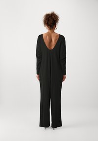 Mono negro de manga larga con diseño de escote en la espalda y forma de pierna ancha, elaborado con tejido suave y liso, que presenta un estilo minimalista.