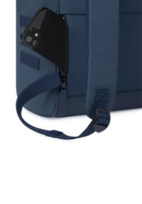 Zaino blu navy in tessuto texturizzato, con una tasca con zip che contiene un telefono nero. Include una tracolla regolabile e accessori robusti.