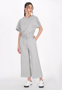 Grijze, geweven set van twee delen met een losvallend top en wijde broek met verstelbare tailleband. Gecombineerd met witte sneakers.