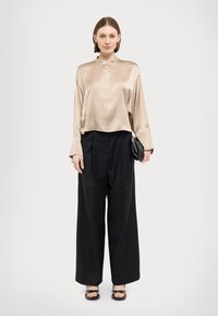 Beige sateng langermet skjorte med høy krage og en enkelt knapp, parret med høytaljede svarte vide bukser. Svart clutch.