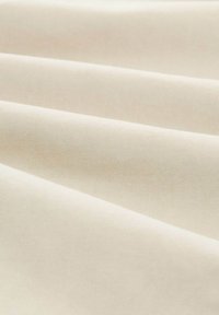 Beige stof met een gladde textuur en diagonaal ribbelpatroon, gevouwen in zachte golven, wat een lichtgewicht en duurzaam materiaal aantoont.
