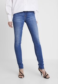 Blå skinny jeans i denimtyg med en slät textur, med urblekta detaljer och midjebyxa, paired med svarta remsandaler.