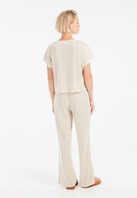 Completo a due pezzi in beige chiaro, composto da una blusa ampia a maniche corte e pantaloni a gamba larga con un motivo a diamante strutturato.
