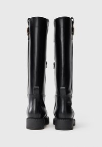 Bottes noires en cuir jusqu'au genou avec une texture lisse, dotées de zips sur les côtés et de talons carrés, avec des coutures détaillées au niveau de la semelle.