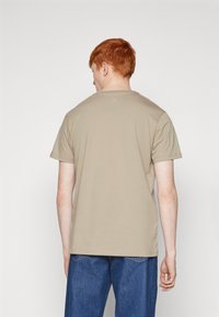 Lichtbeige T-shirt met korte mouwen en een ronde hals, met een zachte katoenen textuur en een relaxte pasvorm. De achterkant toont minimale branding.