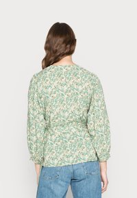 Blusa verde com padrão floral, mangas bufantes e cintura ajustada. Apresenta um decote redondo e um tecido leve e texturizado.