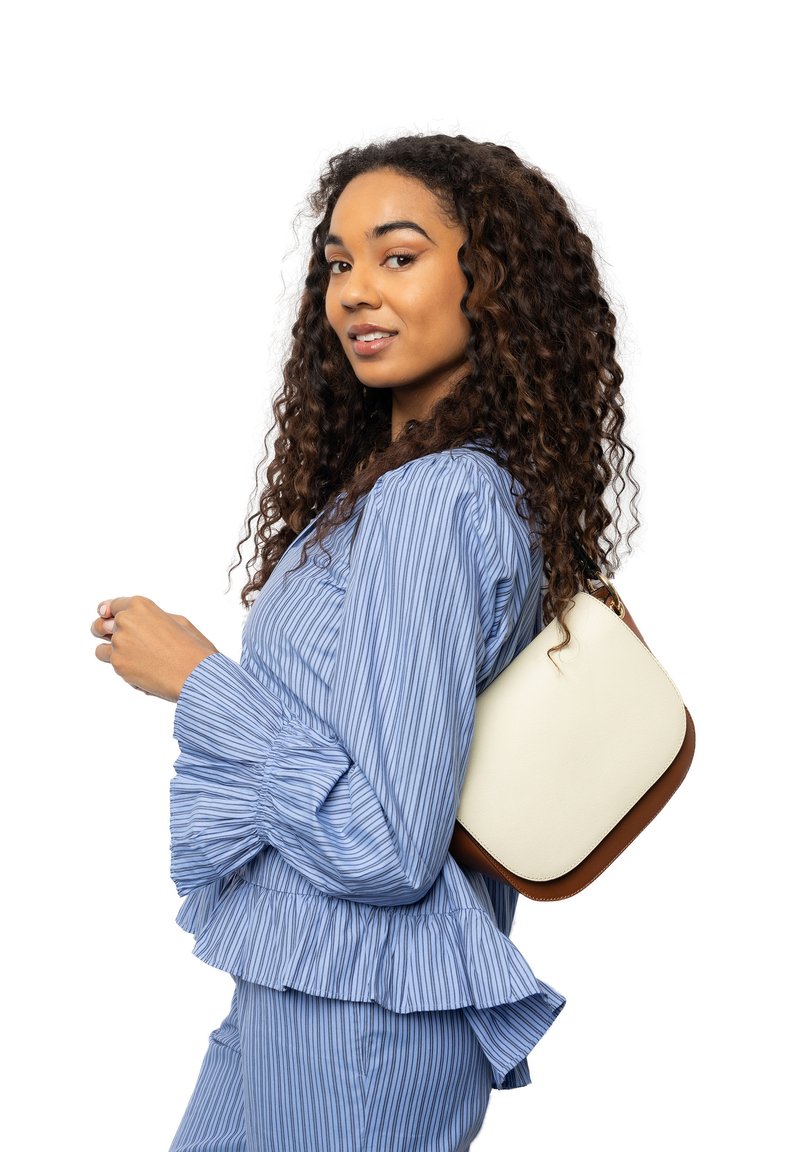 Weißer Handtasche mit braunen Akzenten, rechteckige Form, auf der Schulter gehalten. Das Model trägt eine blaue, gestreifte, rüschenbesetzte Bluse und passende Hose.