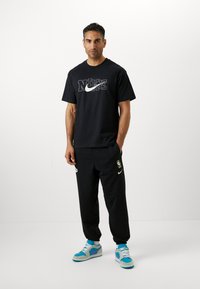 Černé bavlněné tričko s grafikou "NIKE", doplněné černými tepláky s akcentem loga a modrošedými teniskami.