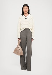 Paksu neulottu kerma sweater mustalla V-kaula-aukolla, yhdistettynä korkeavyötäröisiin harmaisiin ruutuhousuihin. Malli pitää beiget kangaskassia.
