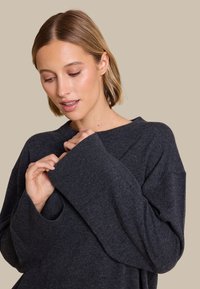 Kullgrå genser med løs passform, vide ermer, ribbestrikkede mansjetter og båtutringning. Myk tekstur, minimale detaljer synlige.