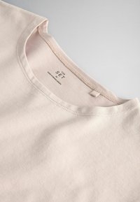T-shirt beige à col rond fabriqué au Bangladesh avec une étiquette visible à l’intérieur du col "THE SET" sur un fond uni clair.