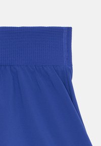 Shorts de sport bleus dotés d'une taille élastique texturée et d'un tissu lisse avec de légers plis au niveau de l'ourlet.