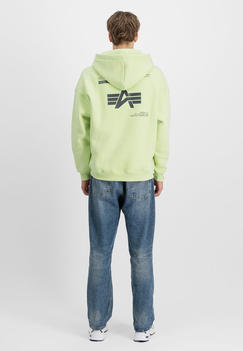 Felpa con cappuccio verde lime, con logo grafico sul retro, tasca a marsupio e polsini a coste; abbinata a jeans baggy azzurri e sneaker.
