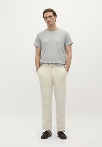 Lichtgrijze ronde hals t-shirt, beige linnen broek met voorkant plooien, bruine veterschoenen, staande tegen een witte achtergrond.