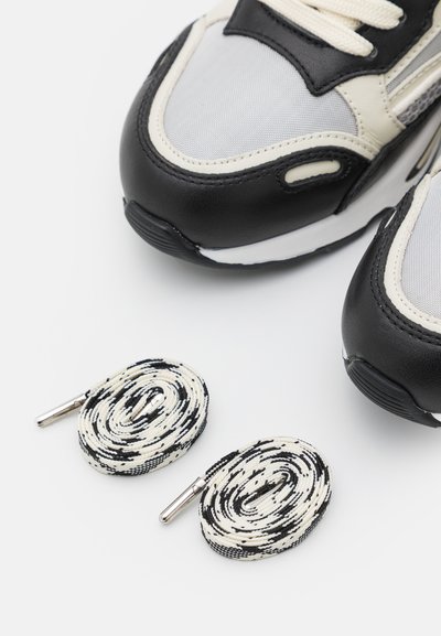 Bottes de sport noires et grises en cuir et en mesh, accompagnées de deux lacets ronds à motifs en noir et blanc avec des embouts en argent.