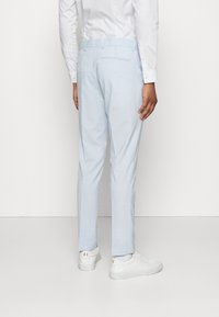 Helle blaue Hosen aus einem strukturierten Stoff, mit einer taillierten Passform, seitlichen Taschen und einem glatten Bund. Kombiniert mit weißen Sneakers.