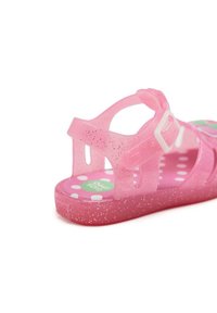 Sandalia de gel rosa con hebilla, con un diseño moteado y plantilla de lunares. El material transparente permite ver el pie.