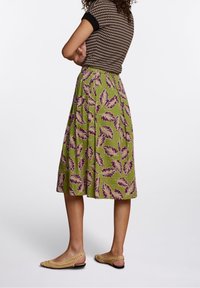 Gonna verde con un motivo a foglia in tonalità viola, lunghezza al ginocchio e una vestibilità comoda. Abbinata a scarpe slip-on in tessuto di un tenue color beige chiaro.