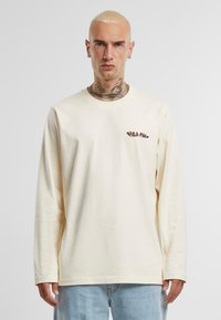 Langemouw T-shirt van zacht crème katoen, met een bruin logo op de linkerkant van de borst, met een ontspannen pasvorm en ronde hals.