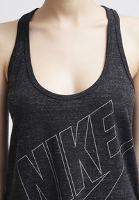 Svart linne gjort av strukturert tyg, med låg rundhals och en stor vit "NIKE"-logotyp över framsidan.