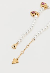 Βραχιόλι με πέρλες και εξαρτήματα σε χρυσό τόνο, με ροζ λεπτομέρειες και τριγωνική γοητεία. Περιλαμβάνει κούμπωμα για ασφαλές κλείσιμο.