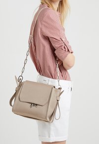 Béžová crossbody taška se strukturovaným designem, klopnou, řetízkovým popruhem a koženými detaily. Hladký povrch a minimalistické kovové prvky.