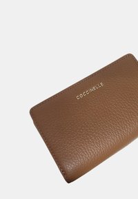 Portafoglio in pelle marrone con una finitura testurizzata, caratterizzato da un logo dorato "Coccinelle" sul davanti e un design pulito e minimalista.