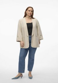Blazer beige oversized avec revers à cran, top sans manches noir, jeans en denim avec ourlets effilochés, et escarpins à bout pointu bleu clair.