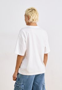T-shirt blanc en coton à coupe décontractée, à manches courtes et à encolure ras du cou. Présente un détail de couture au dos et un design minimaliste.
