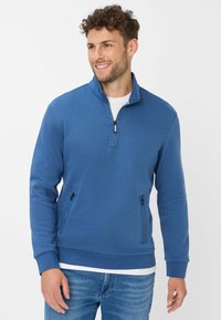Felpa blu con zip, caratterizzata da un colletto alto, maniche lunghe e tasche laterali con zip. Realizzata in tessuto morbido e liscio, con una vestibilità comoda.