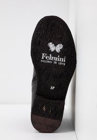 Semelle d'une chaussure en cuir noir avec un logo papillon en relief, "Felmini Falling in Love", et une indication de taille 37, montrant une surface texturée usée.