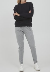 Sweatshirt blu navy con collo a giro, abbinato a joggers grigi chiari a gamba affusolata. Entrambi sono realizzati in tessuto morbido, con scarpe da ginnastica bianche come calzature.