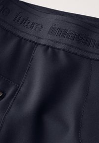 Navy athletic shorts with a smooth texture, featuring an elastic waistband embossed with “the future im agin.” Small side pocket detail.