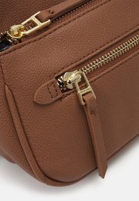 Brown textured leather bag corner with a gold zipper, detailed stitching, and a zipper pull tab. Features visible seams and a smooth finish.