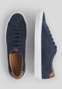 Granatowe zamszowe sneakersy z płaskimi sznurówkami, białą gumową podeszwą i brązowymi skórzanymi akcentami. Charakteryzują się gładką fakturą i prostym, zaokrąglonym kształtem.