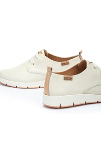 Sneakers bianchi in pelle con una parte frontale in rete testurizzata e dettagli color beige sul tallone. Presentano lacci piatti e una suola in gomma con un leggero plateau.