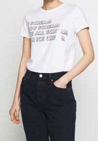 White cotton t-shirt featuring colorful text: "I SCREAM YOU SCREAM WE ALL SCREAM FOR ICE CREAM." Paired with black high-waisted jeans.