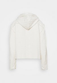 Krótka biała bluza z kapturem, wykonana z teksturowanej tkaniny, z surowymi brzegami i widocznymi przeszyciami z tyłu. Bez kieszeni.