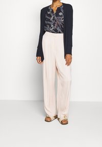 Blusa a fantasia navale, pantaloni larghi color pesca, cardigan scuro, sandali beige con dettagli metallici, vestibilità rilassata, texture morbide.