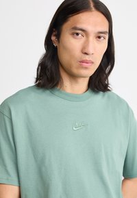 T-shirt verde de manga curta da Nike, feita de algodão suave, com um pequeno logótipo bordado no lado esquerdo do peito.